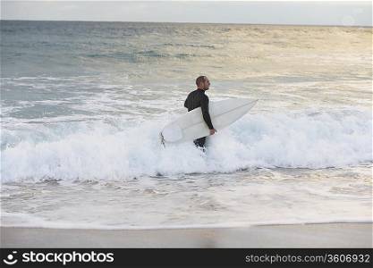Surfer carrying surfboard in sea, side view