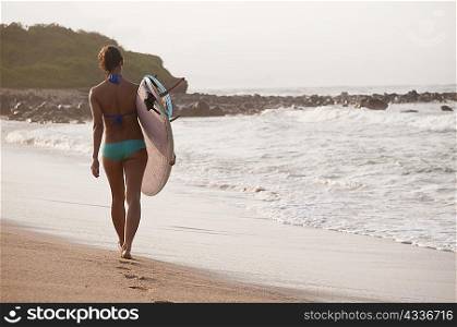 Surfer carrying surfboard on beach