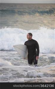 Surfer carrying surfboard out from sea
