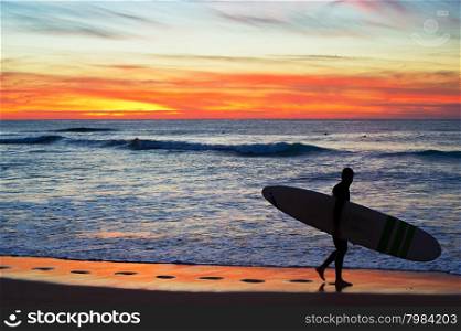 Surfer going away of the beach at dusk. Algarve region, Portugal