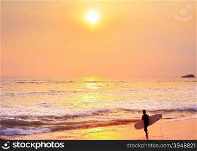 Surfer going to the ocean for surfing at sunset.