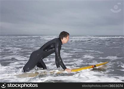 Surfer holding surfboard in water, side view
