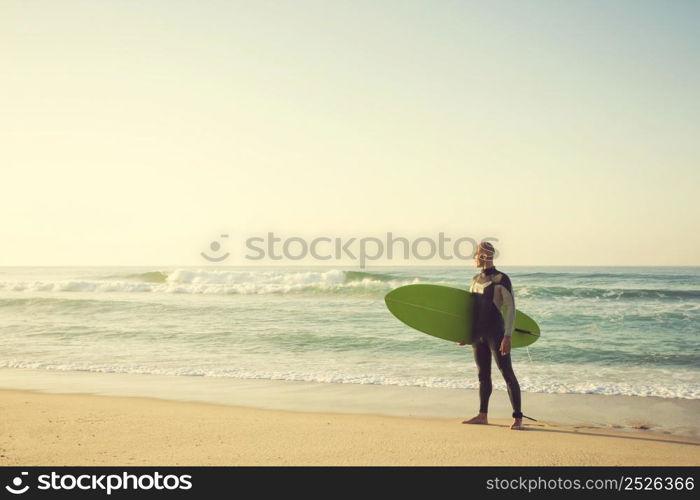 Surfer on the beach holding is surfboaerd and watching the waves