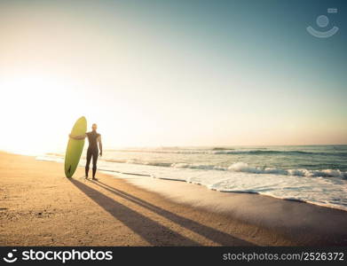 Surfer on the beach holding is surfboaerd and watching the waves