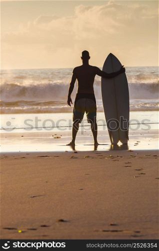 Surfer on the beach holding is surfboard and checking the waves
