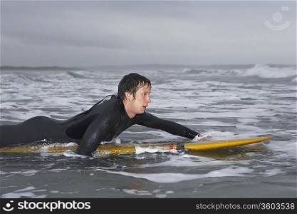 Surfer puddling on surfboard in water, side view
