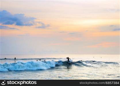 Surfer riding a wave in the ocean at sunset. Bali island