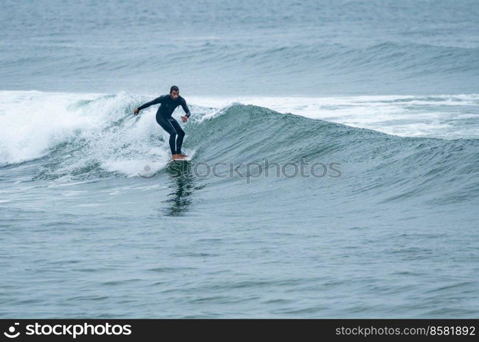 Surfer riding a wave with on a foggy morning in Furadouro beach, Ovar - Portugal.