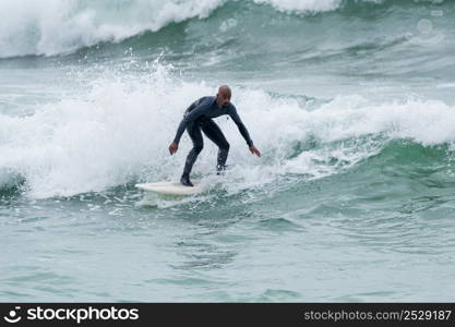 Surfer riding waves with a soft board in Furadouro beach, Portugal. Men catching waves in ocean. Surfing action water board sport.