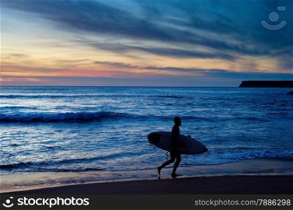 Surfer running with surfboard at dusk. Algarve, Portugal