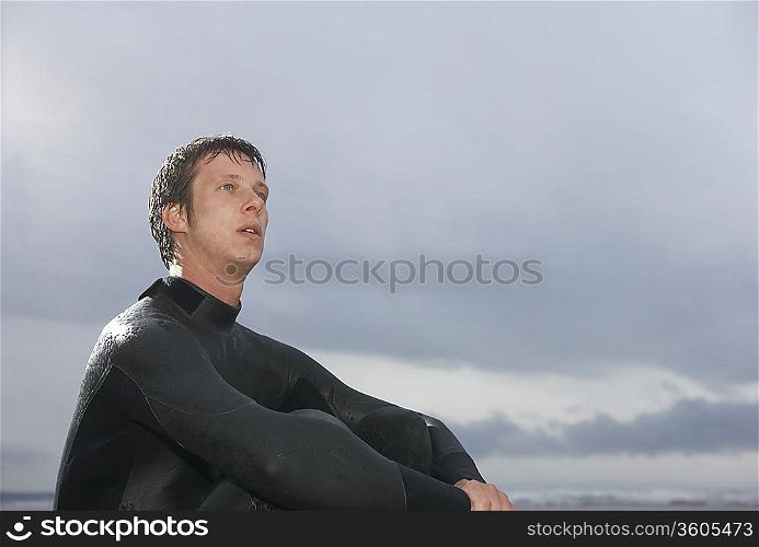 Surfer sitting on beach, low angle view