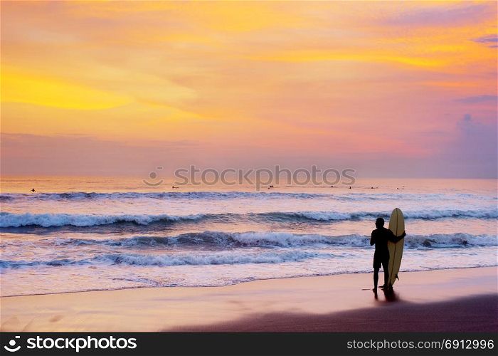 Surfer staying on the beach with surfboard at sunset. Bali island, Indonesia