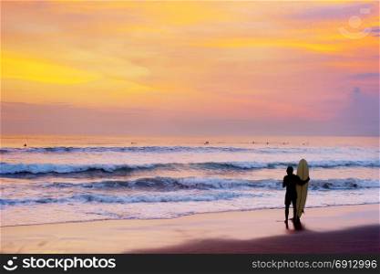 Surfer staying on the beach with surfboard at sunset. Bali island, Indonesia