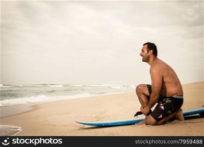 Surfer tying his surfboard&rsquo;s leach on the beach.