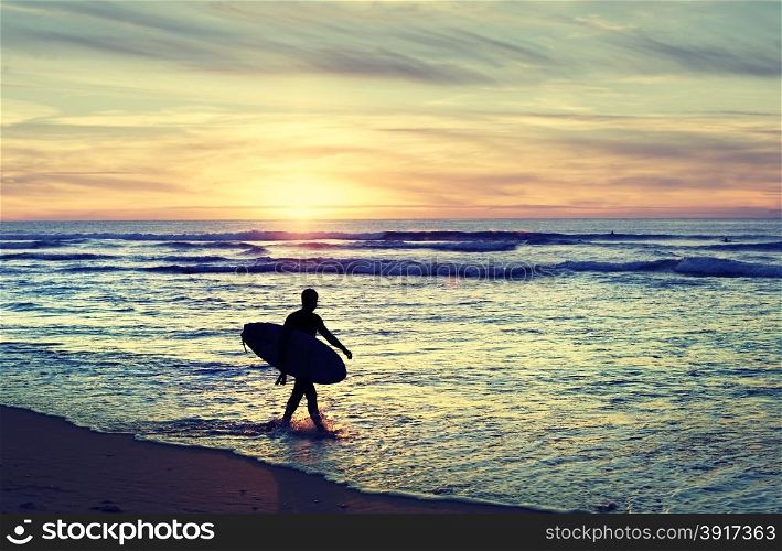 Surfer walking on the beach at sunset. Vintage color