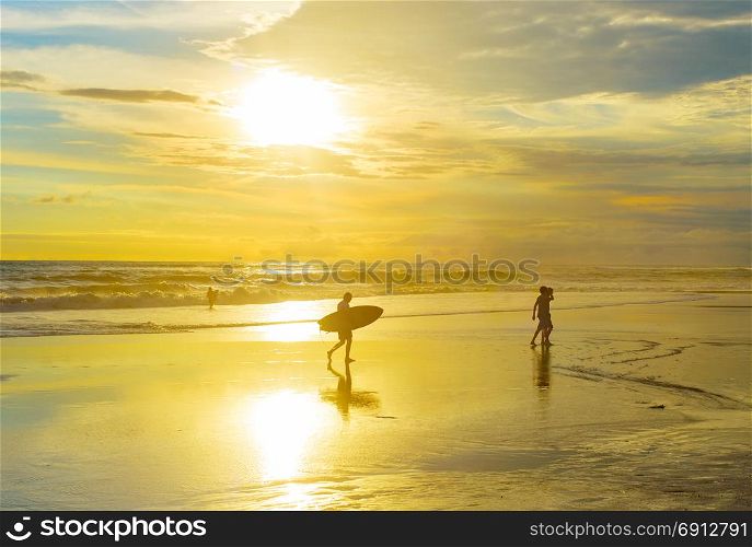 Surfer walking on the beach with surfboard at sunset. Bali island, Indonesia