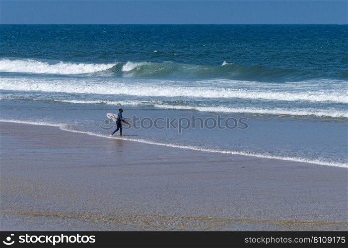 Surfer walking to the sea in Furadouro Beach, Portugal. Men catching waves in ocean. Surfing action water board sport. people water sport lessons and beach swimming activity on summer vacation.