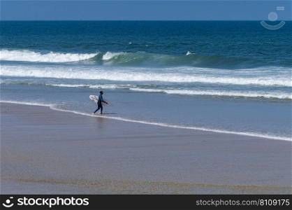 Surfer walking to the sea in Furadouro Beach, Portugal. Men catching waves in ocean. Surfing action water board sport. people water sport lessons and beach swimming activity on summer vacation.
