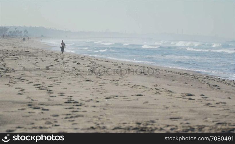 Surfer walks beach near the Santa Monica Pier.