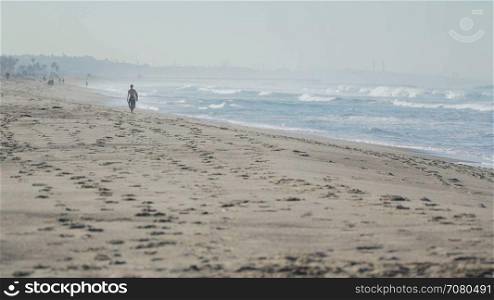Surfer walks beach near the Santa Monica Pier.