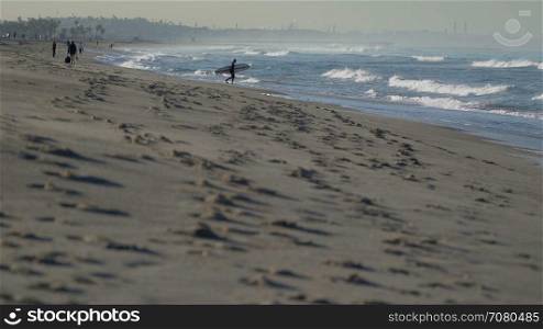 Surfer walks into ocean near the Santa Monica Pier.