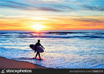 Surfer with surfboard walking on the beach at sunset