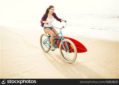 Surfer young woman riding her bicycle on the beach