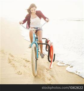 Surfer young woman riding her bicycle on the beach