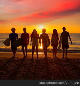 Surfers teen boys and girls group walking on beach at sunshine sunset backlight