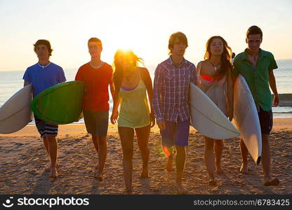 Surfers teen boys and girls group walking on beach at sunshine sunset backlight