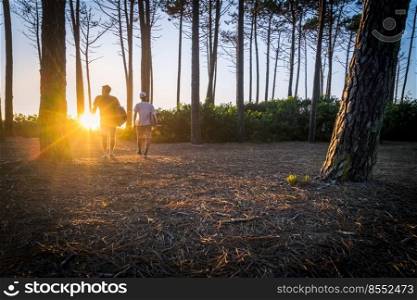 Surfers walking through the pine forest at sunset on top of a sand dune in Maceda, Ovar - Portugal.