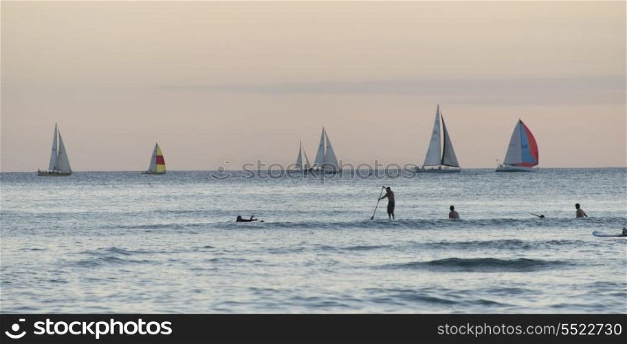 Surfers with sailboats in the background, Waikiki, Honolulu, Oahu, Hawaii, USA
