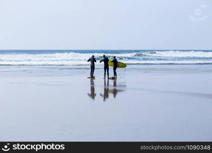 Surfers, with surfboards, on a wet beach in Cornwall, UK