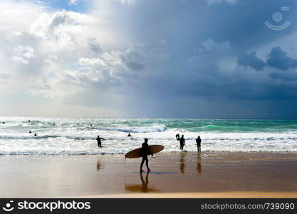 Surfers with surfboards on the beach. Rainy sky. Algarve, Portugal