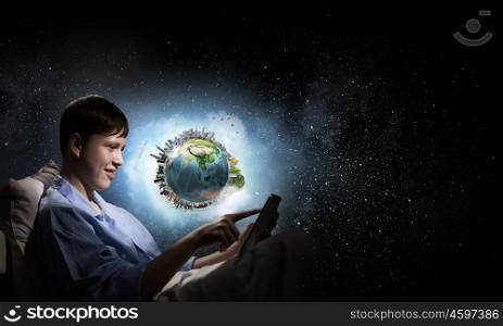 Surfing internet before sleep. Teenage boy in pajamas lying in bed using tablet pc. Elements of this image are furnished by NASA