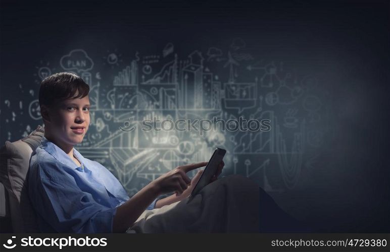 Surfing internet before sleep. Teenage boy in pajamas lying in bed using tablet pc