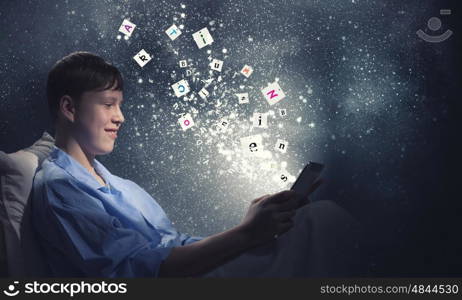 Surfing internet before sleep. Teenage boy in pajamas lying in bed using tablet pc