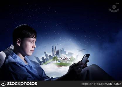 Surfing internet before sleep. Teenage boy in pajamas lying in bed using tablet pc