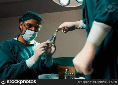 Surgeon fill syringe from medical vial for surgical procedure at sterile operation room with assistance nurse. Doctor and medical staff in full protective wear for surgery prepare anesthesia injection. Surgeon fill syringe from vial for surgical procedure at sterile operation room.