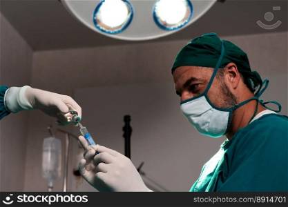 Surgeon fill syringe from medical vial for surgical procedure at sterile operation room with assistance nurse. Doctor and medical staff in full protective wear for surgery prepare anesthesia injection. Surgeon fill syringe from vial for surgical procedure at sterile operation room.