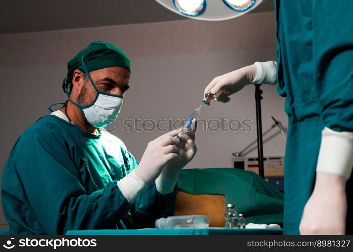 Surgeon fill syringe from medical vial for surgical procedure at sterile operation room with assistance nurse. Doctor and medical staff in full protective wear for surgery prepare anesthesia injection. Surgeon fill syringe from vial for surgical procedure at sterile operation room.