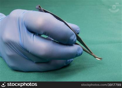 Surgeon holding micro surgical tool.Surgeon hand in blue glove.Surgeon holding Micro-needle holder,curved,short model.The background is blue tablecloth operating