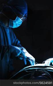 Surgeon looking down, working, and holding surgical equipment with patient lying on the operating table