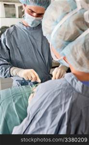 Surgeon with assistant performing operation - live surgery