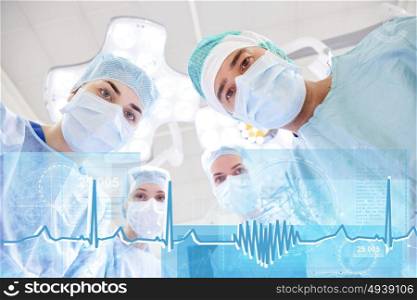 surgery, healthcare, medicine and people concept - group of surgeons in operating room at hospital looking into camera with cardiogram and virtual screen projection. group of surgeons in operating room at hospital