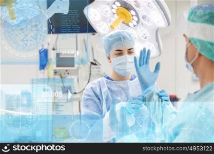 surgery, healthcare, medicine and people concept - nurse assisting surgeon and helping with gloves in operating room at hospital with diagram and virtual screen projection. surgeons in operating room at hospital