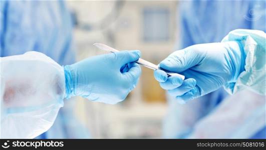 surgery, medicine and people concept - close up of surgeons hands with scalpel at operation in operating room at hospital. close up of hands with scalpel at operation