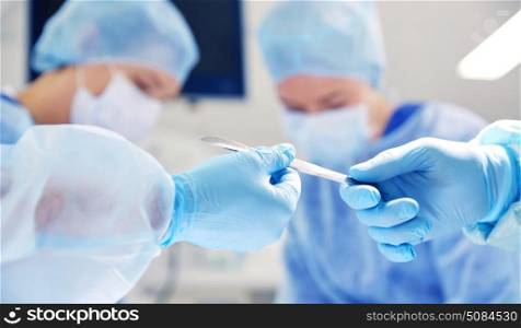 surgery, medicine and people concept - close up of surgeons hands with scalpel at operation in operating room at hospital. close up of hands with scalpel at operation. close up of hands with scalpel at operation