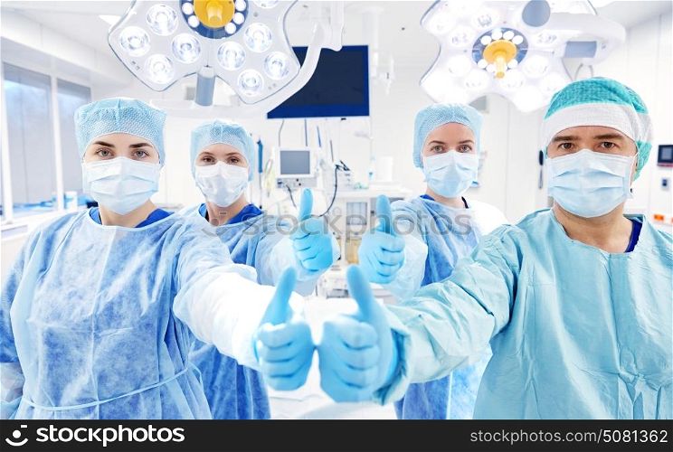 surgery, medicine and people concept - group of surgeons in operating room at hospital showing thumbs up. group of surgeons in operating room at hospital