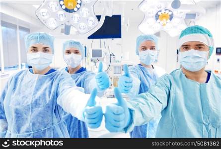 surgery, medicine and people concept - group of surgeons in operating room at hospital showing thumbs up. group of surgeons in operating room at hospital